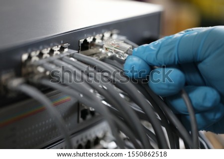 Focus on hand of hardworking man wearing blue glove and plugging high-tech wi-fi chords and ethernet cables used for right work of web router. Computer technology concept. Blurred background