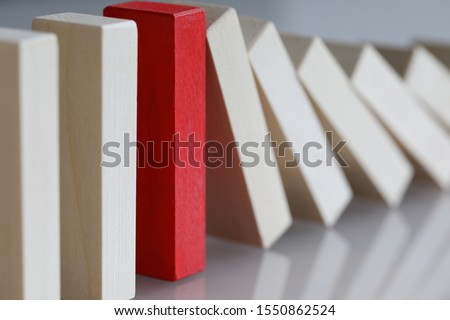 Focus on red object refusing to bend under harsh circumstances affecting other in irreversible sequence of domino effect. One special tile out of many is stopping falling. Strong individual concept Royalty-Free Stock Photo #1550862524