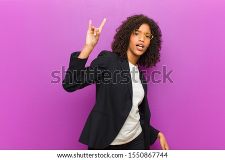 young black business woman feeling happy, fun, confident, positive and rebellious, making rock or heavy metal sign with hand