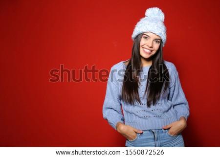 Young woman in warm sweater with hat on red background. Space for text