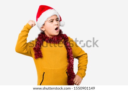 Little boy celebrating christmas day wearing a santa hat isolated raising fist after a victory, winner concept.