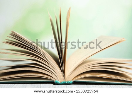 Open book on white wooden table against blurred green background, closeup