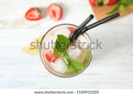 Glass of refreshing drink with strawberry and lime on white table, top view