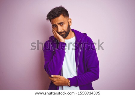 Young indian man wearing purple sweatshirt standing over isolated pink background thinking looking tired and bored with depression problems with crossed arms.