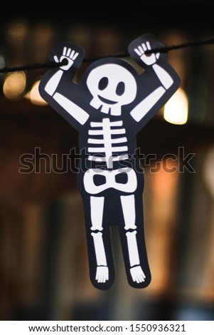 Cute White skeleton bone hanging by black rope with bokeh blurred background, halloween holiday festival concept. 