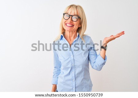 Middle age businesswoman wearing elegant shirt and glasses over isolated white background smiling cheerful presenting and pointing with palm of hand looking at the camera.