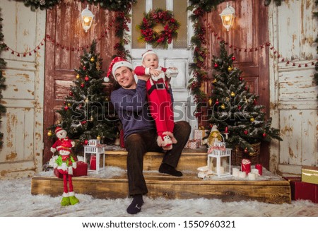Happy dad in Santa hat plays with his little son dressed as Santa Claus on the background of New Year interior.