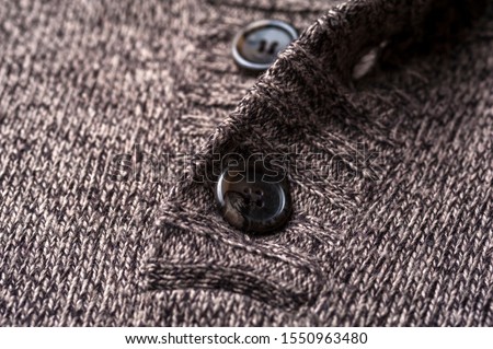 Close-up of a gray knitted warm jacket with black buttons lies on the table. The concept of warm autumn-winter things. Knitwear for body warm concept
