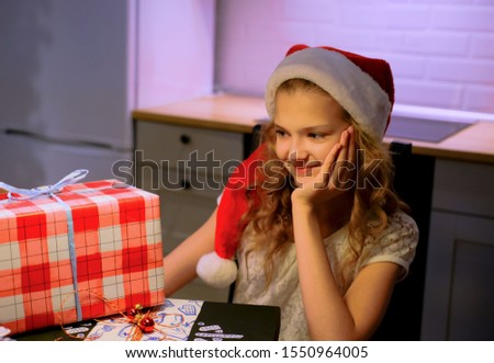 Young cute girl sitting at a table with Christmas gifts. young lady is wrapping gifts. Girl opens gifts. Home decor in the background. Concept: Christmas shopping.
