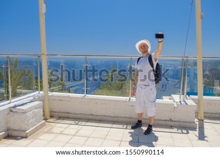 tourist in a white hat and white clothes makes selfie phone on the background of panorama of mountains and the sea