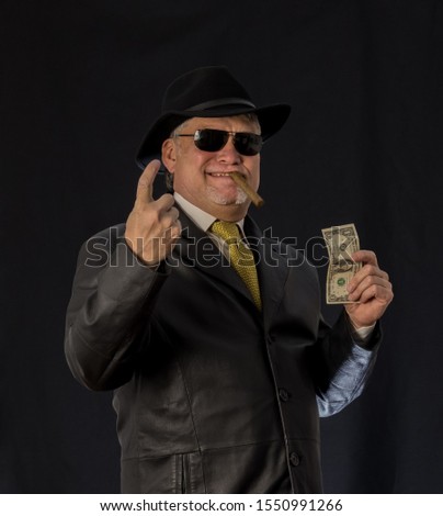 A man in black clothes, a black leather coat, hat. Ganster with a cigar. Mafiosi in black glasses on a dark background. Severe, strong, stylish, impressive, dangerous, unfriendly, evil, rude man.