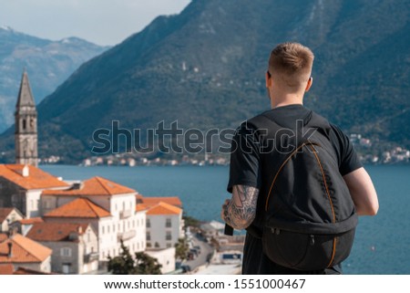 Young stylish man traveler with big backpack enjoying of old european town of Montenegro view