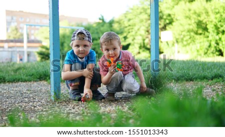 Two cute little kids squatting on the playground playing with toys.