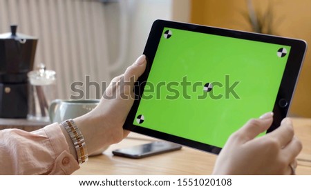 Close-up of beautiful young woman working in tablet with green screen. Stock footage. Female hands hold and hold on green screen of tablet. Working on tablet as freelancer