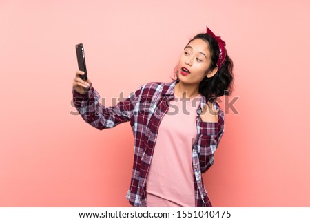 Asian young woman over isolated pink background making a selfie