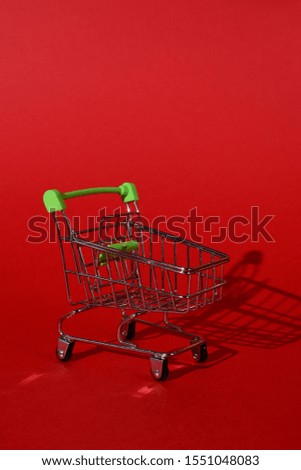 small empty metal trolley from a supermarket on a red background. Hard directional light, clear shadow from the cart. Horizontal photo.trading concept.