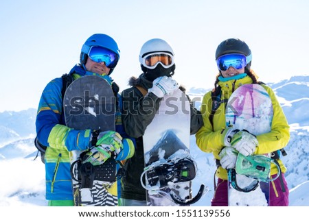 Photo of three athletes wearing helmets and snowboards in hands at snow resort.