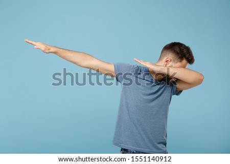 Young man in casual clothes posing isolated on blue wall background, studio portrait. People sincere emotions lifestyle concept. Mock up copy space. Showing dab dance gesture
