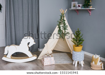 Rocking horse for children made of phoners and cardboard in a children's room decorated for Christmas or New Year, a wigwam tent for children and an artificial Christmas tree