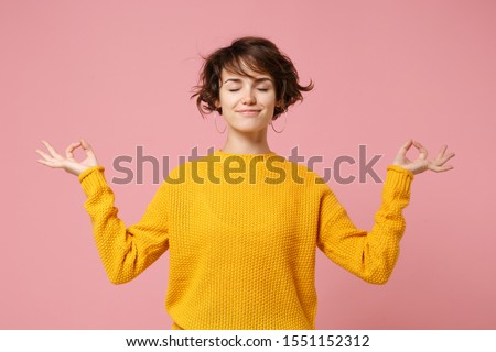 Young brunette woman girl in yellow sweater posing isolated on pastel pink background. People lifestyle concept. Mock up copy space. Hold hands in yoga gesture relaxing meditating keeping eyes closed