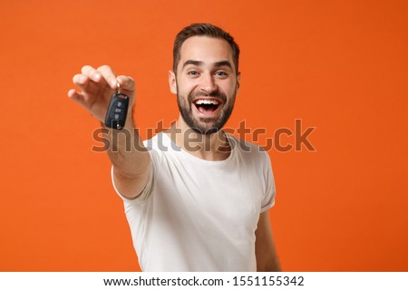 Excited young man in casual white t-shirt posing isolated on bright orange wall background studio portrait. People sincere emotions lifestyle concept. Mock up copy space. Holding in hand car keys