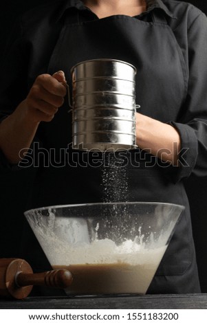 The cook is working making the dough, sprinkle flour in a bowl on a black background. Freezing in motion. Cooking baking, culinary background, recipe book, menu. Vertical frame
