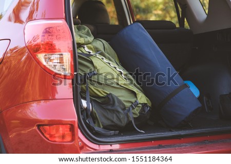 Green backpack and karemat in cover packed for travel outdoors. Touristic equipment at open car back boot.