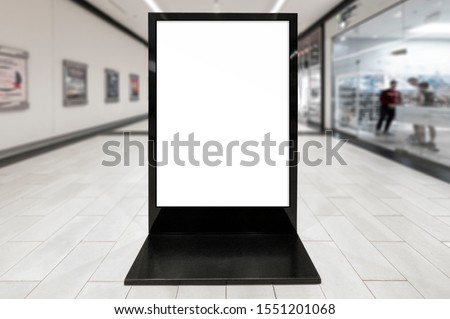 Mockup of blank white vertical indoor advertising poster stand with black frame in shopping centre or mall