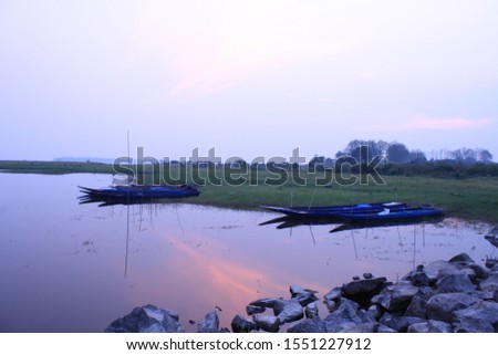 
A photo of a boat parked by fishermen catching fish in a large lagoon in the setting sun. Nature background