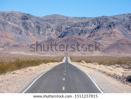 Empty road bisects desert valley as it travels towards mountains. Highway called Old Spanish Trail