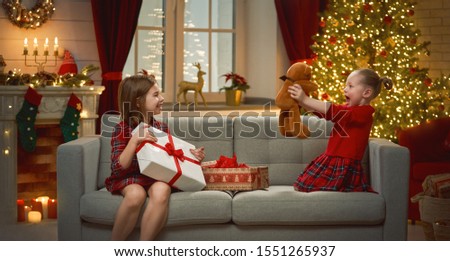 Merry Christmas and Happy Holidays! Cheerful cute childrens girls opening gifts. Kids are having fun near tree in the morning. Loving family with presents in room.