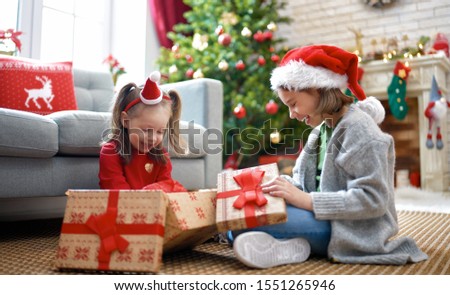 Merry Christmas and Happy Holidays! Cheerful cute childrens girls opening gifts. Kids are having fun near tree in the morning. Loving family with presents in room.