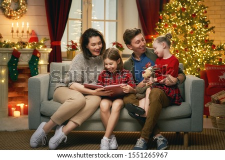 Merry Christmas! Pretty young mother reading a book to her daughters near Christmas tree. 
