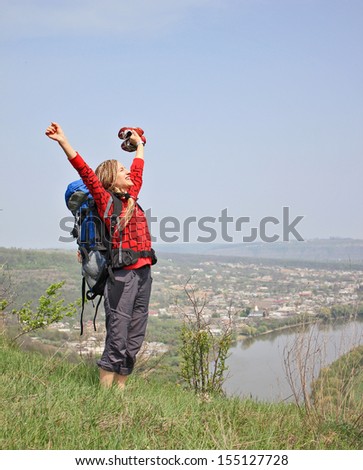 Young Happy Girl with African Braids and with Backpack Standing on Rock near Big River with raised hands