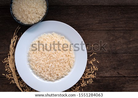 Parboiled Rice uncook in dark ceramic color and paboiled rice cooked in a white ceramic plate placed on a wooden table. Parboiled rice close up shot. Parboiled rice top view. Royalty-Free Stock Photo #1551284063