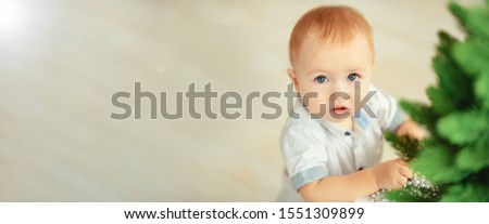 Baby and Christmas. A small blond boy in blue jeans and a white shirt stands at a table with. Banner. New Year background