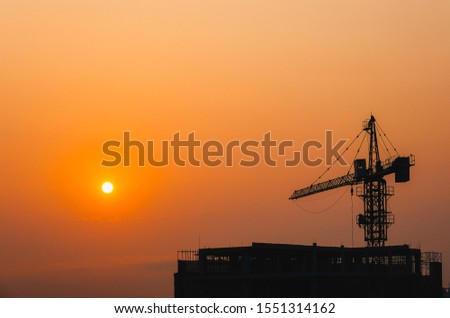 Crane building construction site at sunset or sunrise. Stock photo image silhouette of construction tower crane in sunset sky background and the sun. Building construction with crane during sunset
