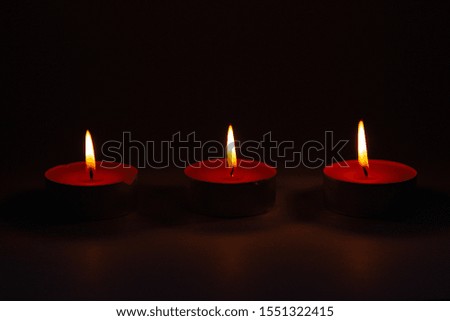 Three small pink wax decorative candles burn on a dark background. Front view.