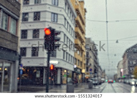 Rain. Cold rainy day in the city. Drive. Poor weather conditions. Red traffic light. Overcast. Shower. Bad visibility on roads. Perspective. Blurred avenue scene. Drops of rain. Blur urban background.