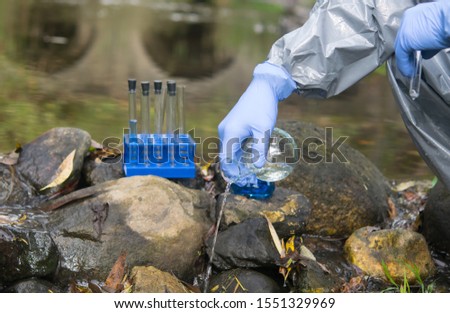 scientist's hand, in a protective suit and gloves, pours liquid from a flask into a pond
