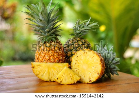 Group of sliced and half of pineapple(Ananas comosus) on wooden table with blurred garden background.Sweet,sour and juicy taste.Have a lot of fiber,vitamins C and minerals.Fruits or healthcare concept Royalty-Free Stock Photo #1551442142