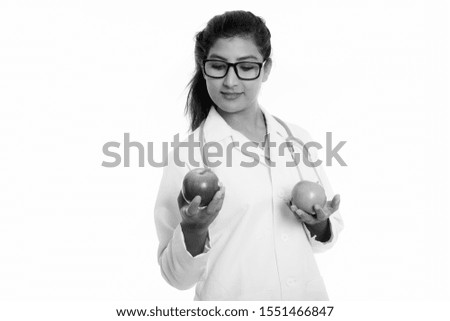 Studio shot of young beautiful Persian woman doctor looking at red apple and holding green apple