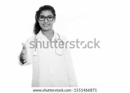 Studio shot of young happy Persian woman doctor smiling while giving handshake