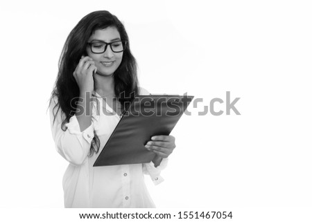 Young happy Persian woman smiling while talking on mobile phone and reading on clipboard