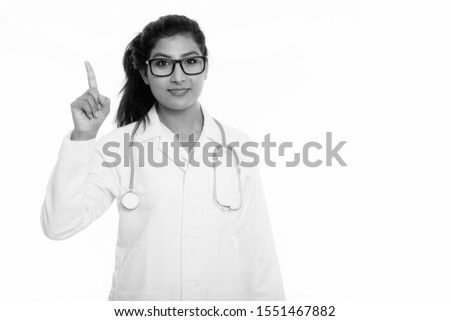 Studio shot of young happy Persian woman doctor smiling while pointing finger up