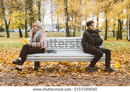 Two teenagers in love in a quarrel. A brunette boy and a blonde girl are sitting on opposite ends of the benches, their backs to each other, do not want to talk and talk. Teenage Difficulty Concept Royalty-Free Stock Photo #1551500060