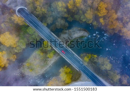Aerial photo of misty and moody autumn landscape with red vehicle in the middle of the frame