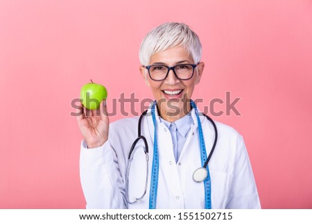 Portrait of mature smiling female nutritionist holding an apple isolated. Nutritionist with healthy fruit, juice and measuring tape. Dietitian working on diet plan.