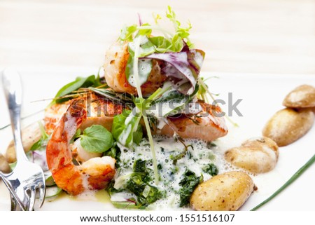 Salmon filet with scampi on a bed of spinach with potatoes in their skins and creamy wine sauce