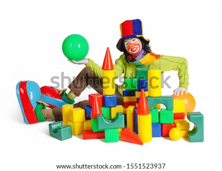     Sitting female clown with painted face in hat and big boots. A lot of geometric cubes. Studio shot.                           